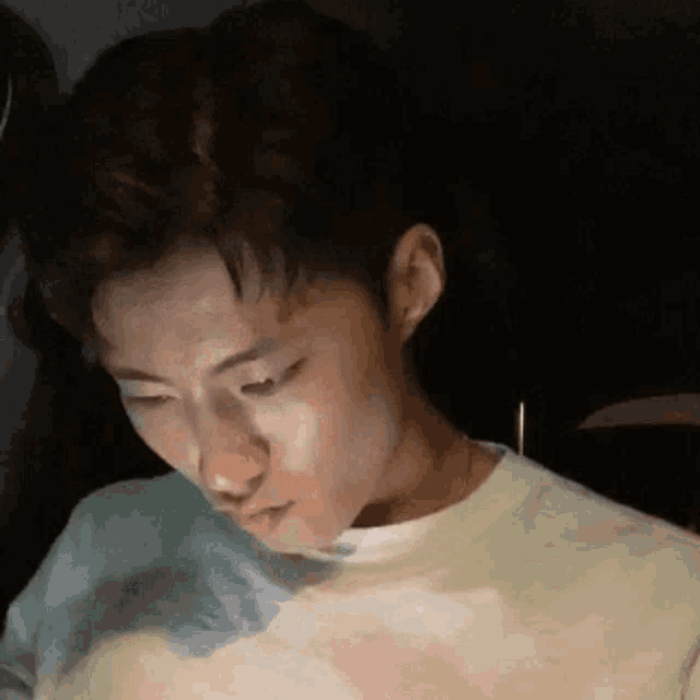 a young man is sitting in a dark room with his eyes closed and looking down .
