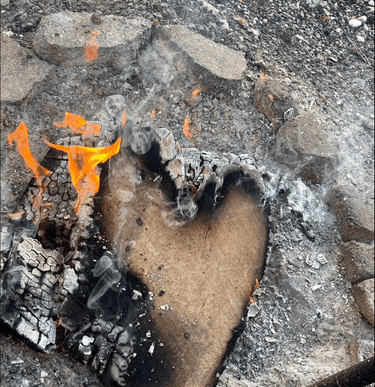 a heart shaped piece of wood burns in a fire pit