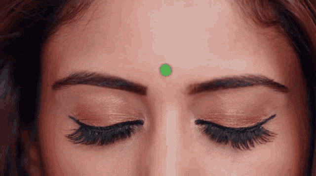 a close up of a woman 's face with a green bindi on her forehead