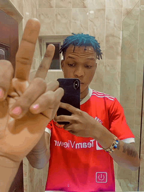 a man taking a picture of himself in a mirror wearing a red shirt that says ' tweiv meet ' on it