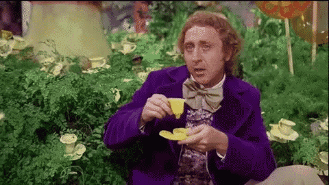 a man in a purple suit and bow tie is sitting in a garden holding a yellow cup of tea .