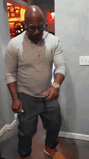 a man wearing sunglasses and a gray shirt stands in a hallway