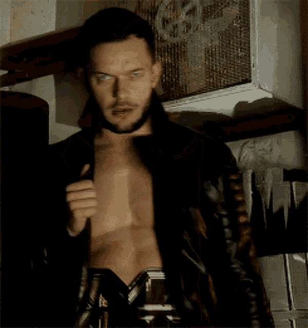 a shirtless man with a beard is wearing a black jacket over his shoulder