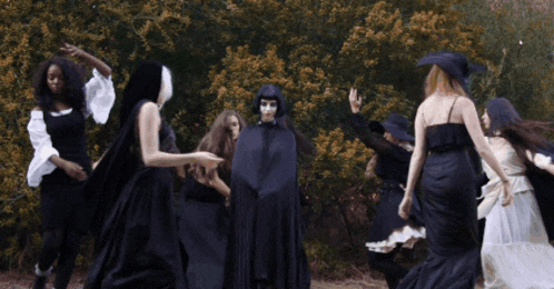 a group of women in black dresses are dancing in a forest