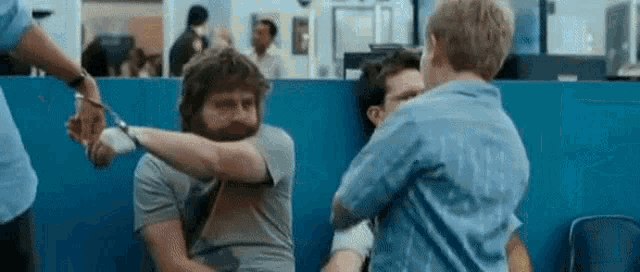 a man with a beard is being handcuffed by a police officer while a boy hugs him .