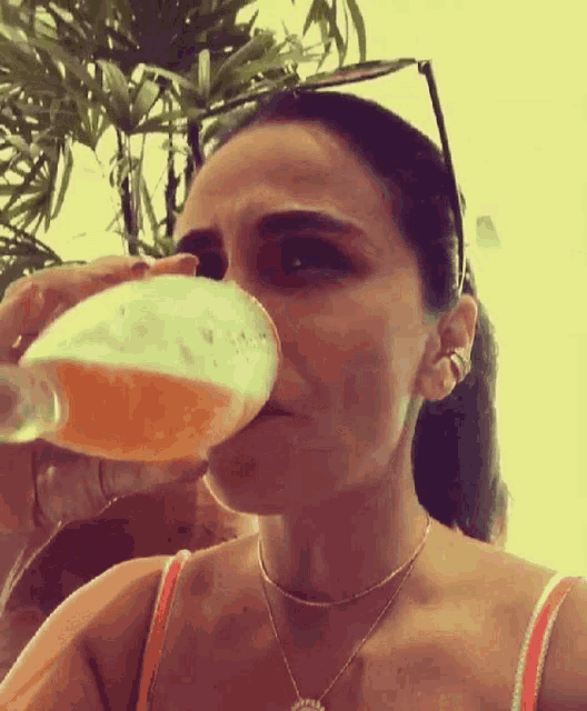 a woman is drinking a glass of beer from a bottle while wearing sunglasses
