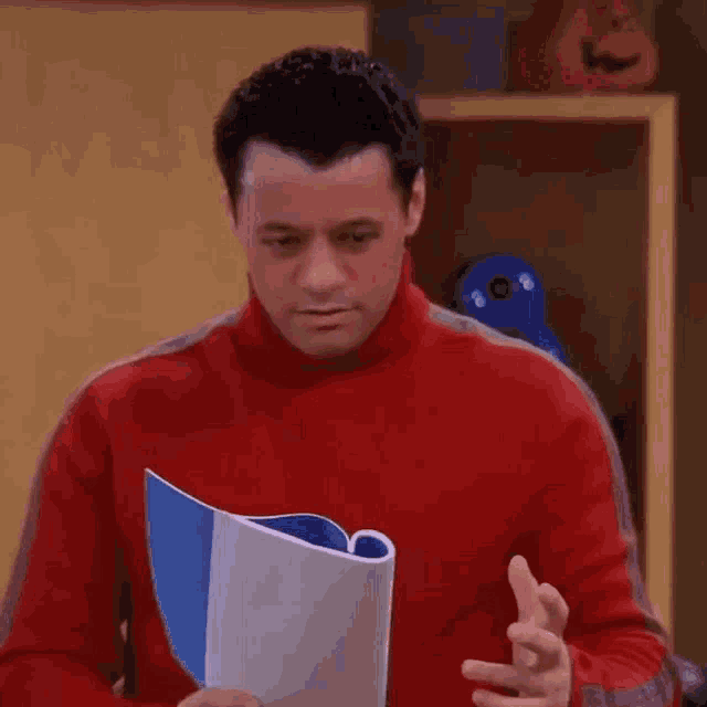 a man in a red sweater is holding a book in his hands .