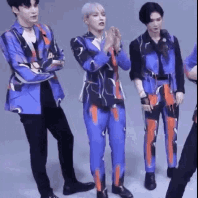 a group of men in blue and orange suits are standing next to each other and clapping their hands .