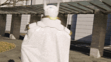 a person in a white cape with horns on their head stands in front of a building