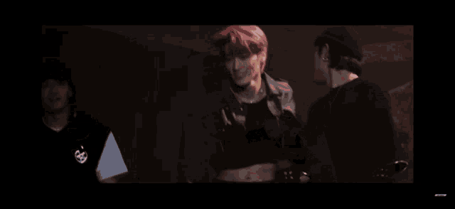 a young man with pink hair is standing in a dark room .