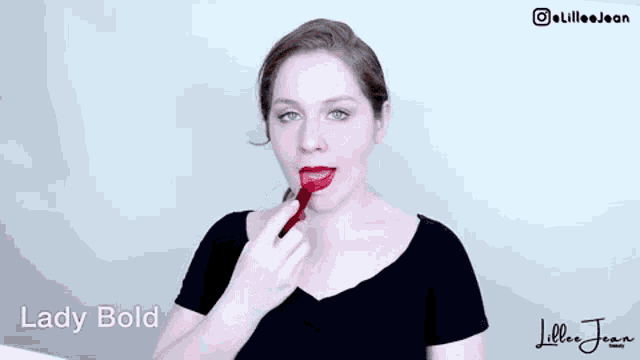 a woman wearing a black shirt is applying red lipstick to her lips .