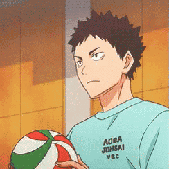 a man in a blue shirt is holding a volleyball in his hands .