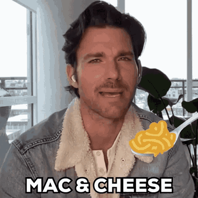 a man in a denim jacket is holding a spoon full of macaroni and cheese .