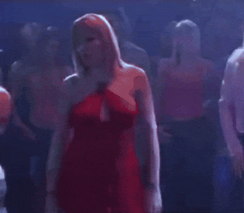 a woman in a red dress is standing in a crowd of people