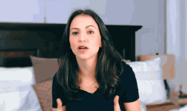 a woman in a black shirt is standing in front of a bed making a funny face