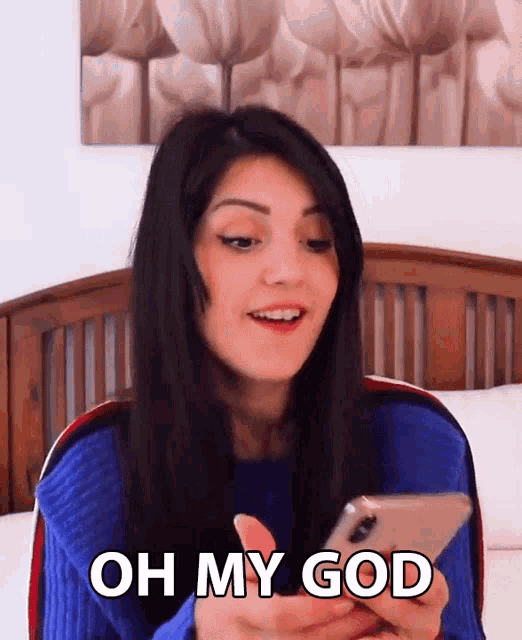 a woman in a blue sweater is looking at her phone and saying oh my god