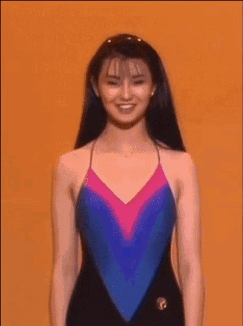 a woman in a swimsuit is smiling while standing in front of an orange background .