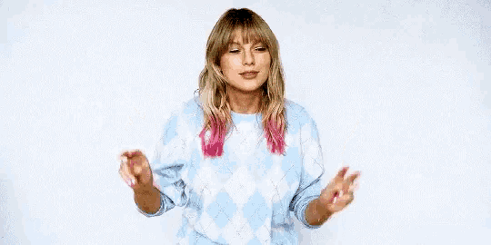 taylor swift is wearing a blue and pink plaid sweater and giving a peace sign .