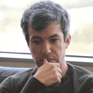 a man with gray hair is sitting in front of a window with his hand to his chin