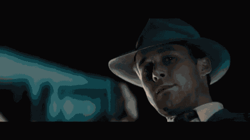 a man wearing a hat and tie is holding a gun in his hand .