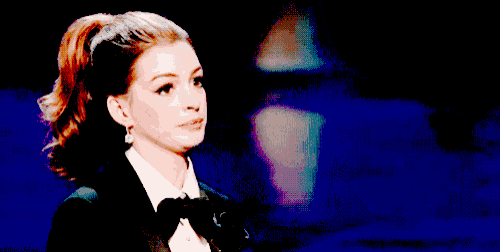 a woman wearing a tuxedo and bow tie looks to the side