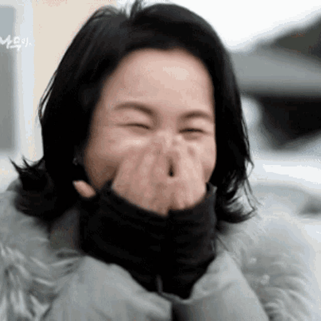 a woman in a fur coat is laughing with her hands over her mouth