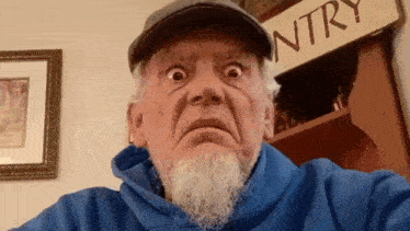 an elderly man with a beard and hat is making a funny face .