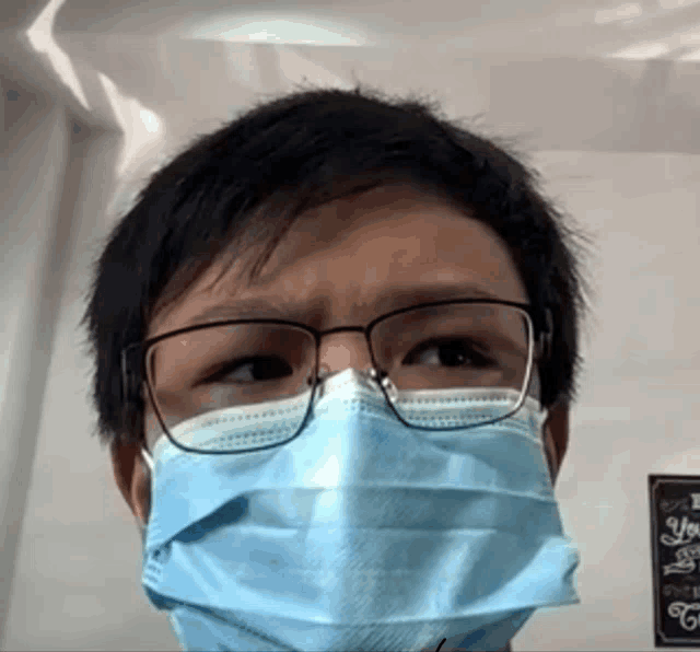 a man wearing glasses and a blue face mask looks at the camera