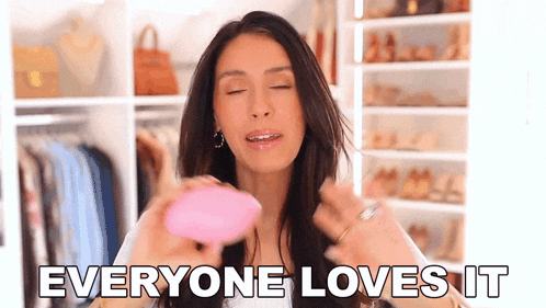 a woman is holding a pink object in front of a closet and says everyone loves it .