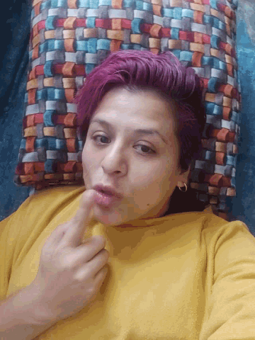 a woman with pink hair and a yellow shirt is laying on a couch