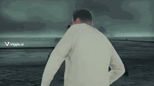 a man in a white sweater is standing in front of a body of water with a viggle.ai logo on the bottom right