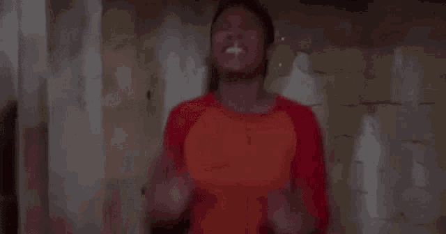 a woman in an orange shirt is standing in front of a wall with her arms in the air .