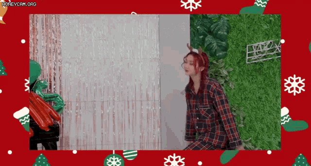 a woman wearing a plaid shirt and antlers is standing in front of a christmas backdrop .