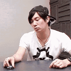 a man wearing a hat and a white shirt is sitting at a table playing with a toy car