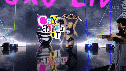 a woman holding a wrestling championship stands in front of a sign that says " cry about it "
