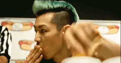a man with green hair is eating a hot dog while a referee watches .
