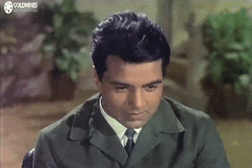 a man in a suit and tie is sitting in front of a screen that says goldmines