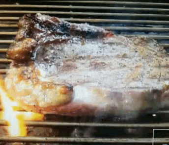 a large piece of meat is cooking on a grill with flames