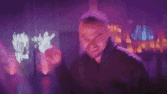 a man in a black hoodie is making a funny face in a dark room with purple lights behind him .