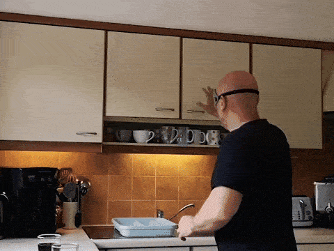 a man in a black shirt is standing in a kitchen reaching into a cabinet