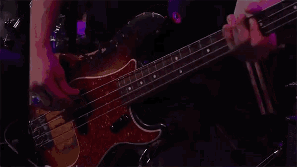 a person is playing a bass guitar in a dark room with purple lights .