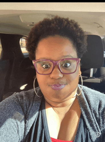 a woman wearing glasses and hoop earrings is sitting in the back of a car