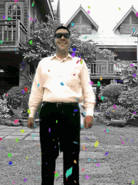 a man wearing sunglasses is standing in front of a house with confetti falling around him