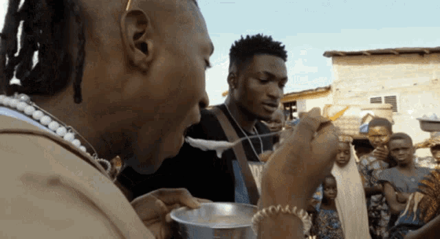 a man with dreadlocks is holding a spoon in his mouth while another man looks on