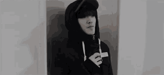 a black and white photo of a young man wearing a hoodie and a baseball cap .