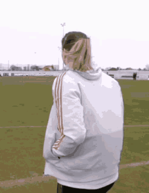a woman is standing on a soccer field wearing a white jacket with red stripes .