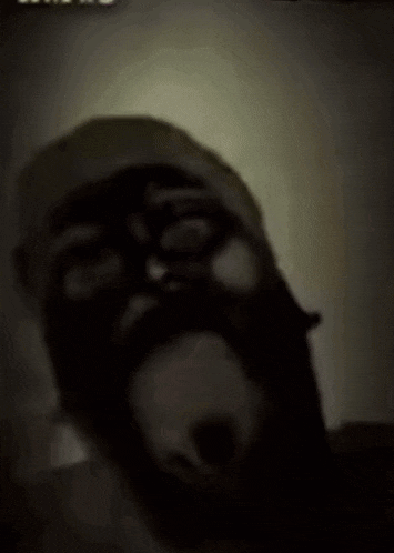 a man with a beard and a mask on his face is making a funny face in the dark .