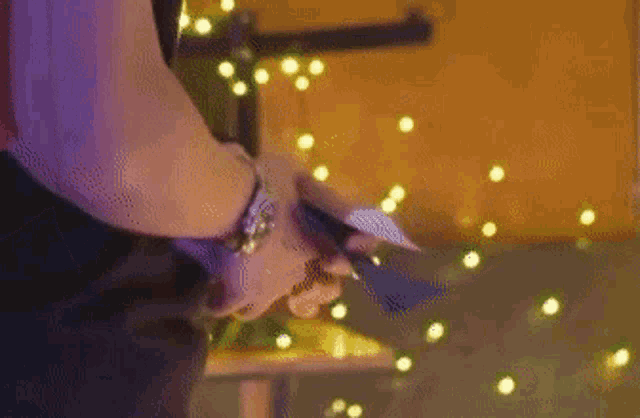 a person is cutting a piece of paper with a knife in front of christmas lights .