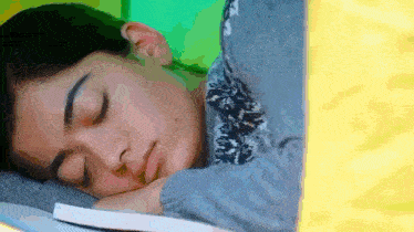 a young woman is sleeping on a book with her head on a pillow .