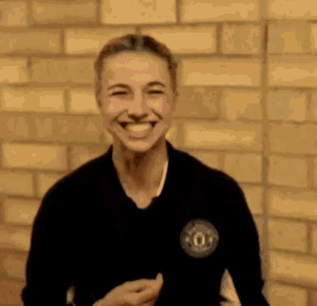 a woman is smiling in front of a yellow brick wall .